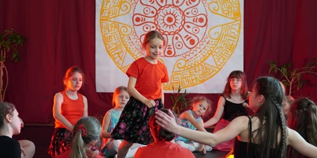 Powiększ grafikę: Na scenie młodzi artyści siedzą w kręgu i wirują wokół ogniska.