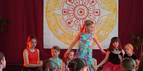 Powiększ grafikę: Na scenie młodzi artyści siedzą w kręgu i wirują wokół ogniska.
