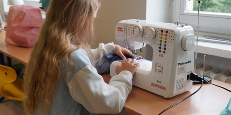 Powiększ grafikę: Dziewczynka szyje na maszynie. Do pracy wybrała niebieską tkaninę.