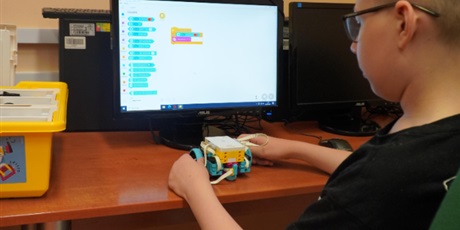 Powiększ grafikę: Chłopiec pokazuje efekt pracy z zajęć robotyki. W tle komputer.