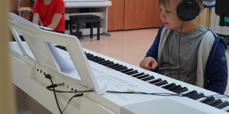 Powiększ grafikę: Chłopiec w słuchawkach gra na elektrycznym białym pianinie.