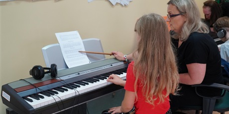 Powiększ grafikę: Nauczycielka wskazuje dziewczynce nuty i uczy ją grać na pianinie.