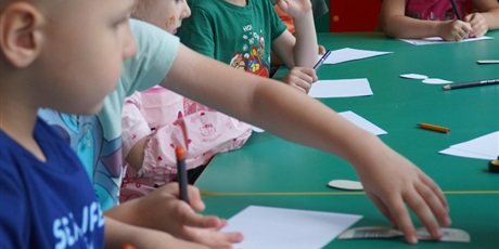 Powiększ grafikę: Dzieci przygotowują się do malowania portretu. N stole leżą kartki i kredki.